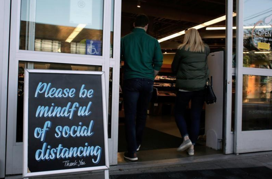 FILE PHOTO: Shoppers enter a grocery store near a sign requesting social distancing, following reports of coronavirus disease (COVID-19) cases in the area, in Seattle, Washington, 